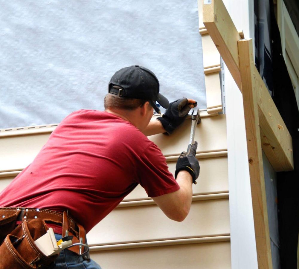 Man in red shirt repairing a wall siding