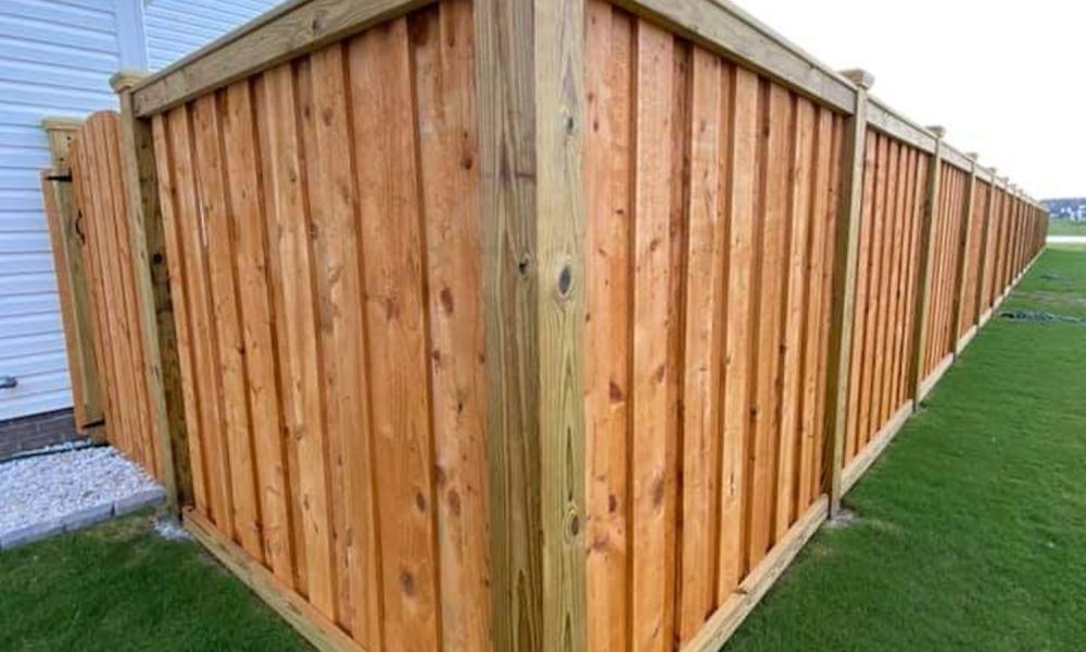 Wooden backyard fence with a corner view, standing on green grass, adjacent to a white house.